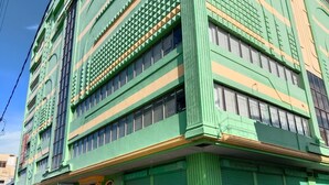 A multi-story building with a green facade, a sign for the Meaco Royal Hotel, and several parked cars. - Meaco Royal Hotel- Lucena (Lucena)