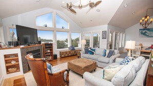 A spacious living room with a large TV, comfortable seating, and a fireplace. - Oceanside, ELEVATOR, Indoor-Outdoor pool, Sauna, Rec Room, Media Room, BH12, Celtic Tides (Corolla)