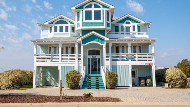 A two-story building with a balcony, a staircase leading to the entrance, and a garage. - Oceanside, ELEVATOR, Indoor-Outdoor pool, Sauna, Rec Room, Media Room, BH12, Celtic Tides (Corolla)