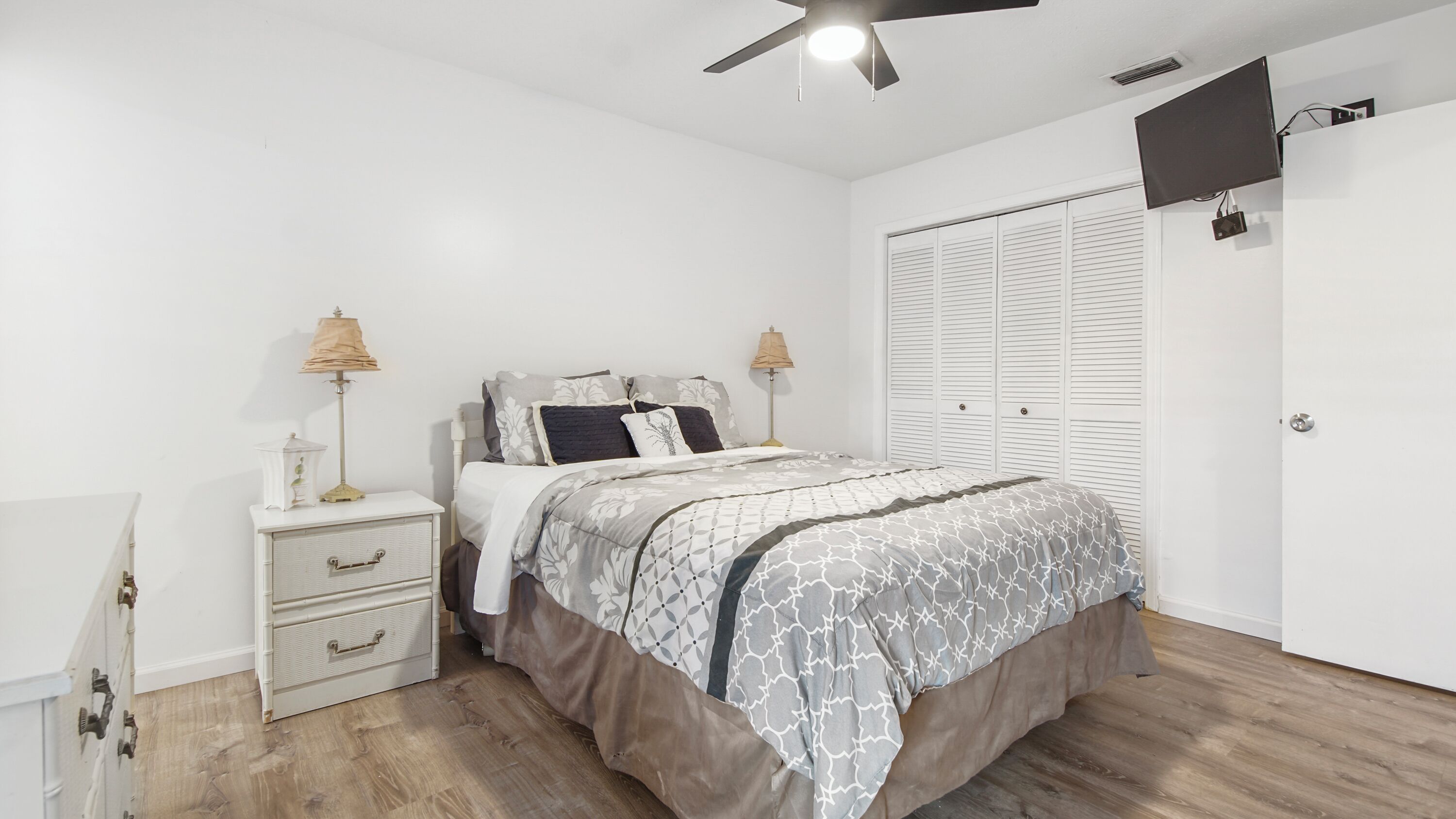 Une chambre à coucher avec un lit, des lampes de chevet, une armoire et un ventilateur de plafond.