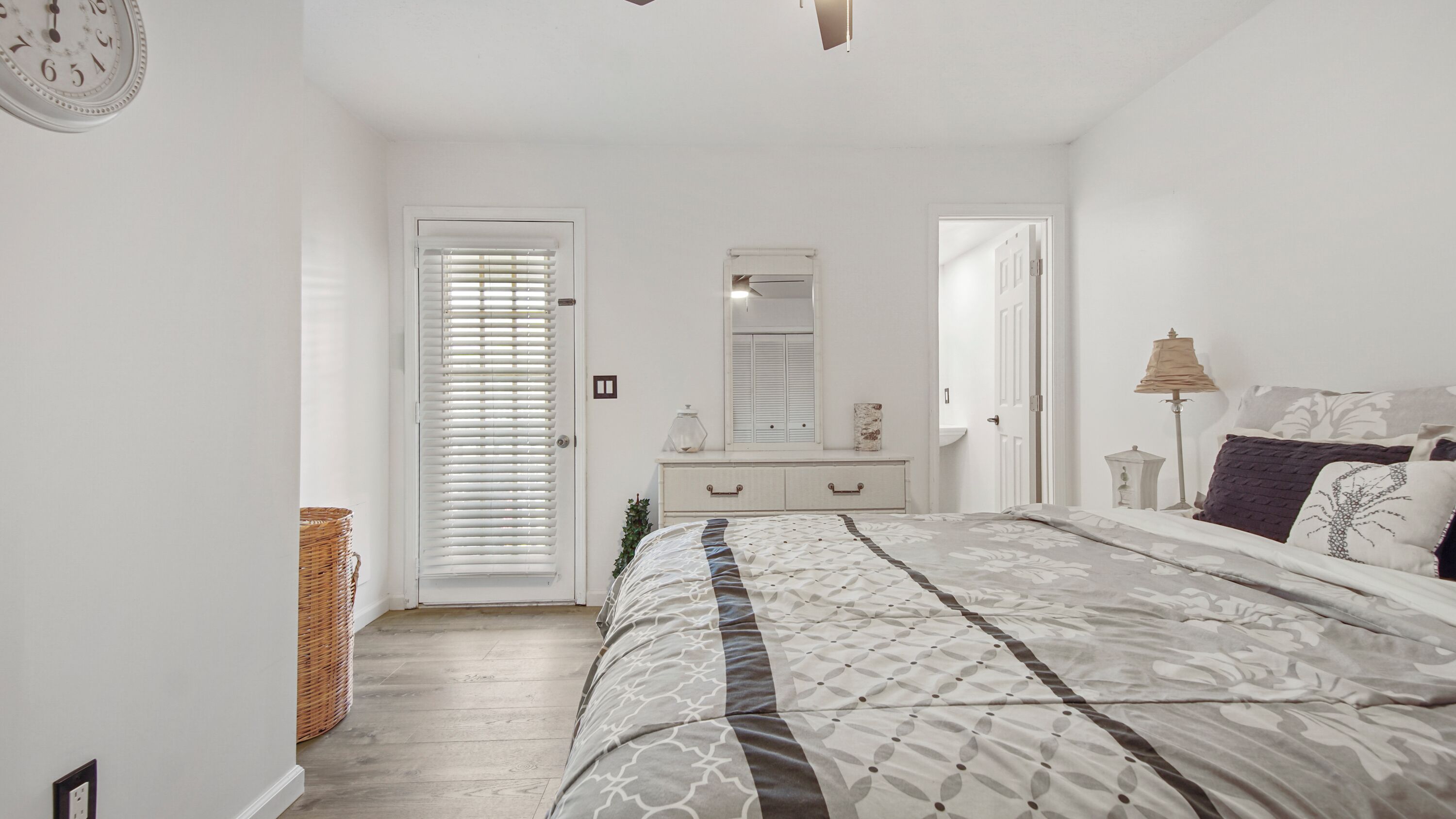 A bedroom with a bed, dresser, mirror, and a door with blinds.