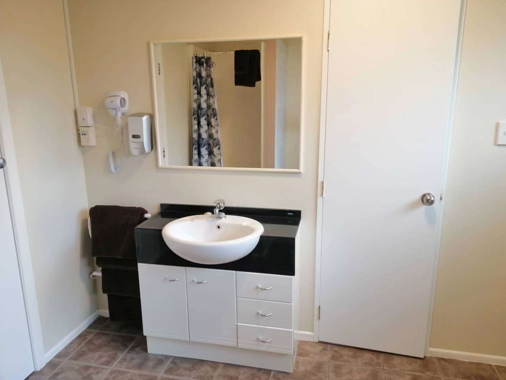 A bathroom with a white sink, black countertop, and a mirror above it. There is a towel rack and a hand dryer on the wall.