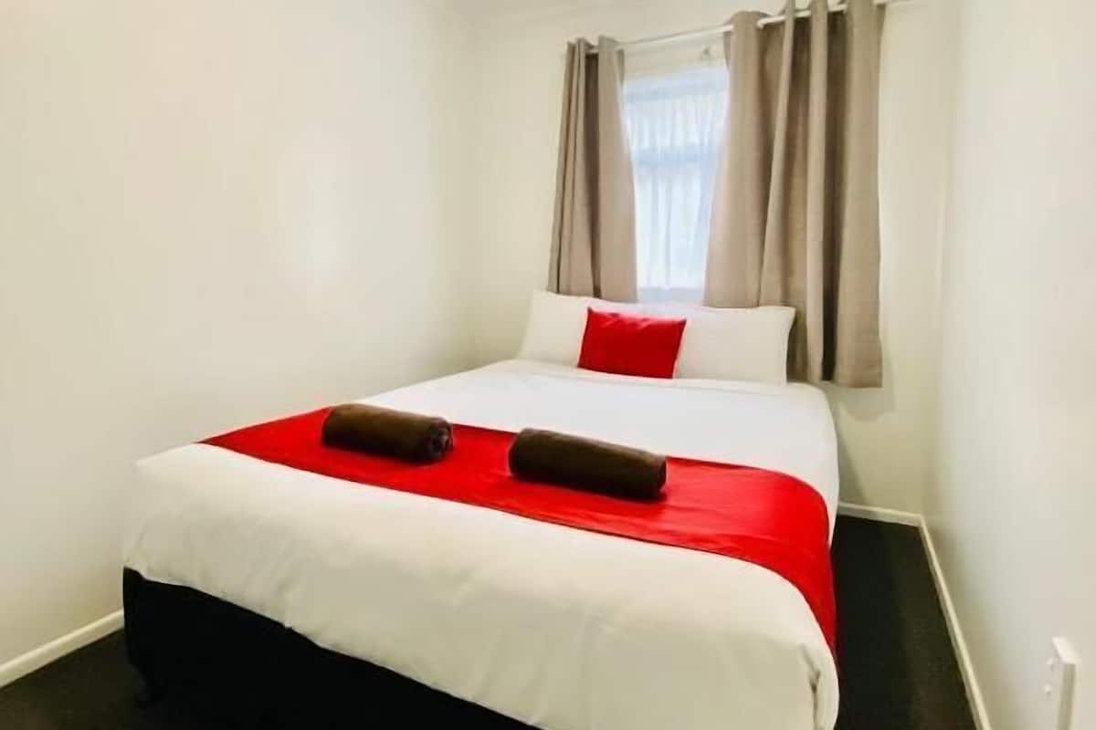 Una habitación de hotel con una cama, un ventanal con cortinas y una lámpara en el techo.
