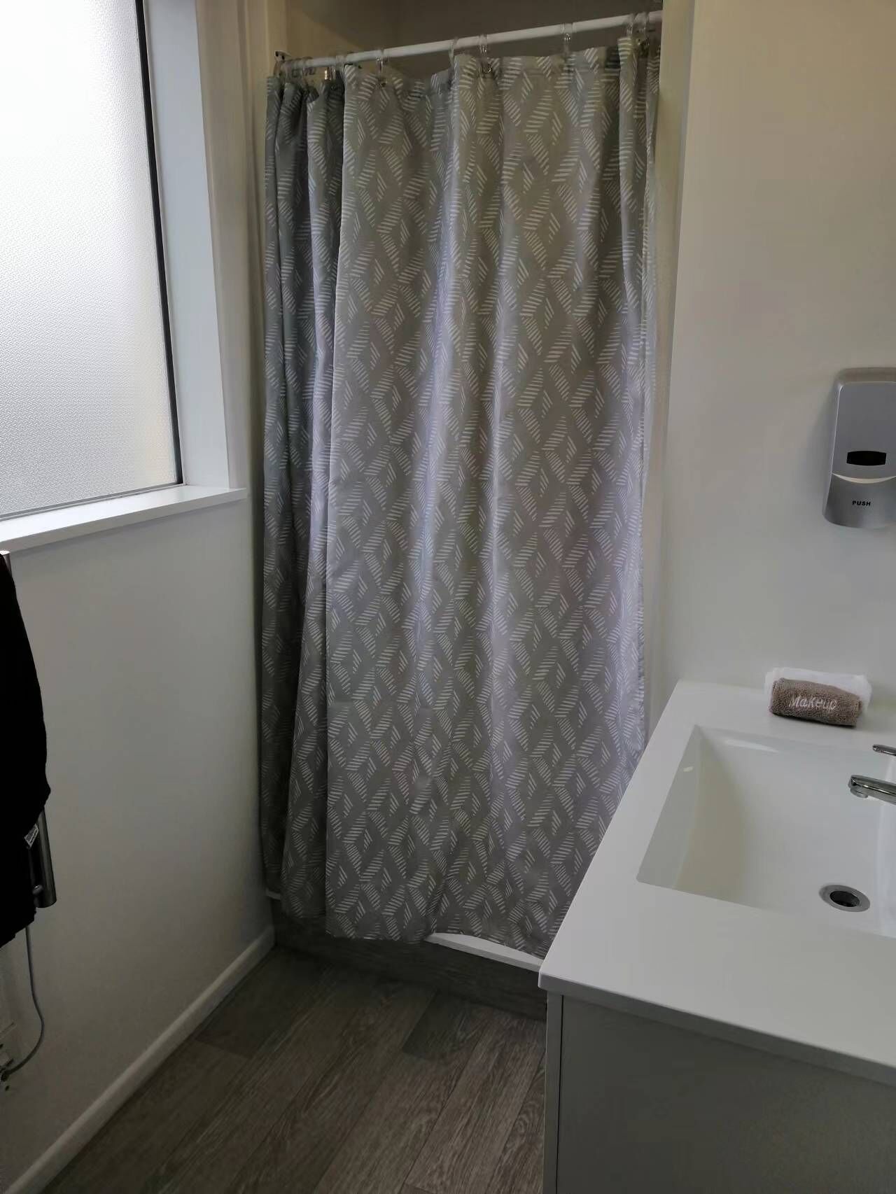 A bathroom with a shower curtain, a sink, and a soap dispenser.