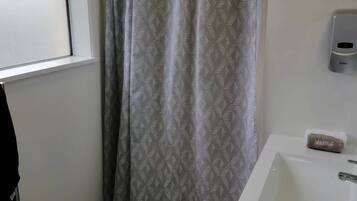 A bathroom with a shower curtain, a sink, and a soap dispenser.
