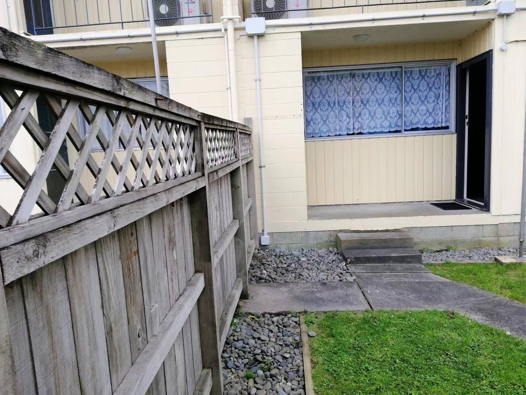 A residential building with a wooden fence, a concrete pathway, and a small grassy area.