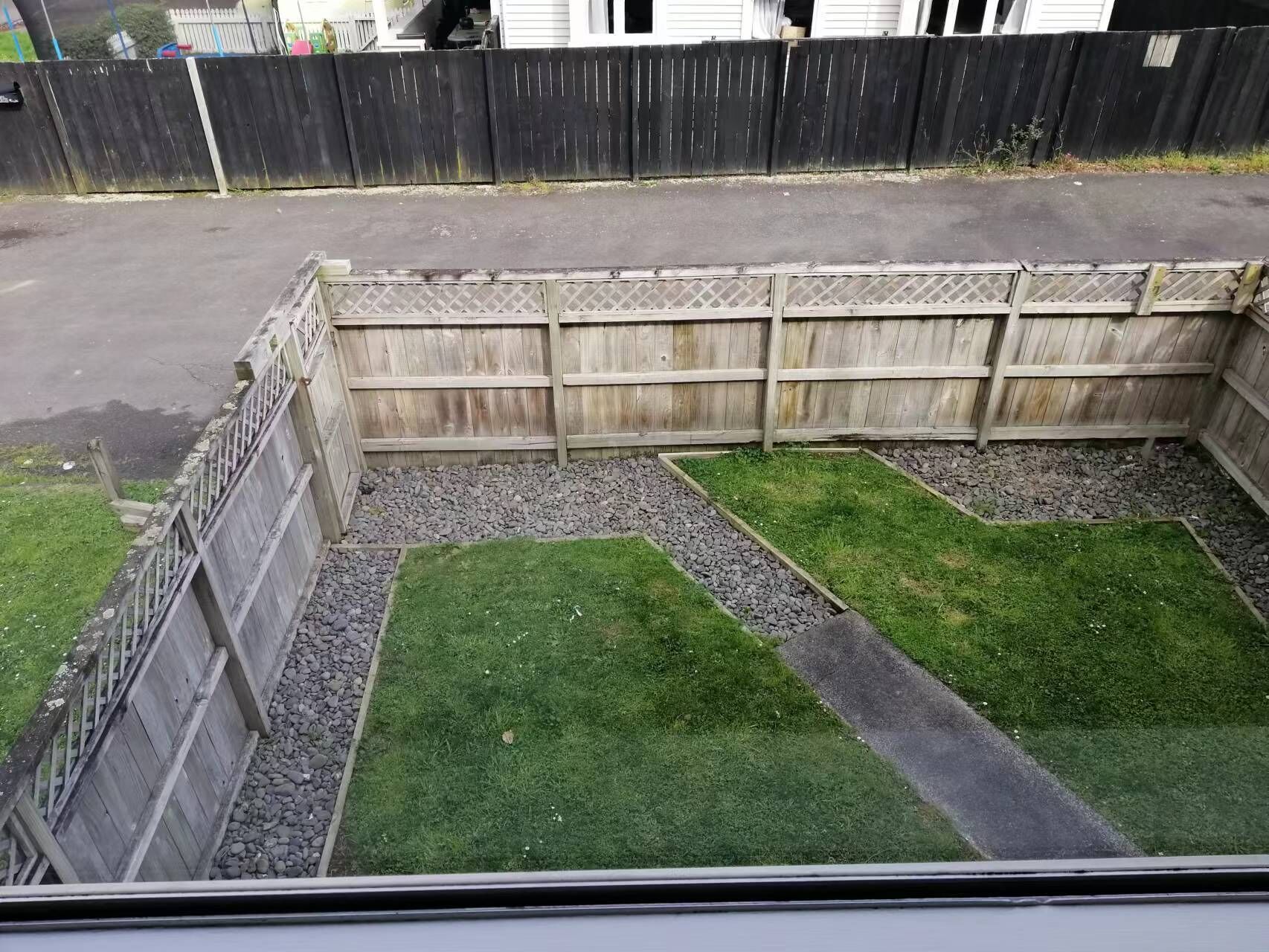Un cortile recintato con un vialetto sterrato e prato.