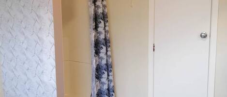 A bathroom with a white door, a shower curtain with a floral pattern, and a marble-patterned wall.