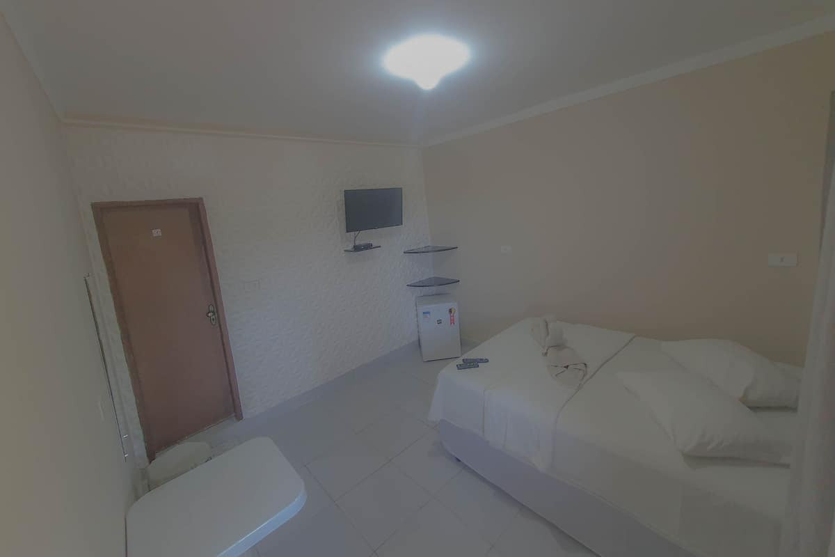 Une petite pièce propre, avec un lit, un téléviseur fixé au mur, un petit réfrigérateur et une porte.