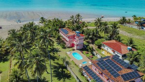 Una propiedad frente a la playa con piscina, paneles solares y palmeras.