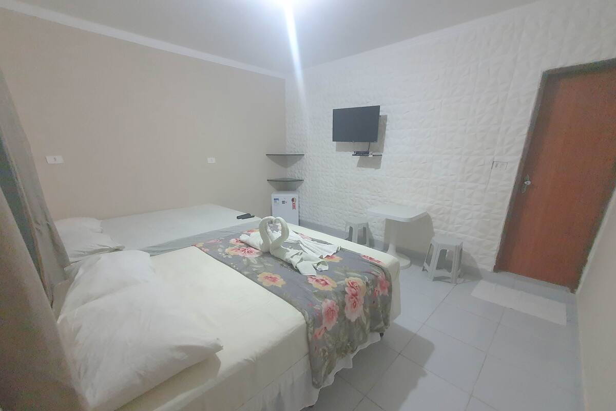 Une chambre d’hôtel avec un lit, un bureau, une chaise, un téléviseur fixé au mur et une porte.