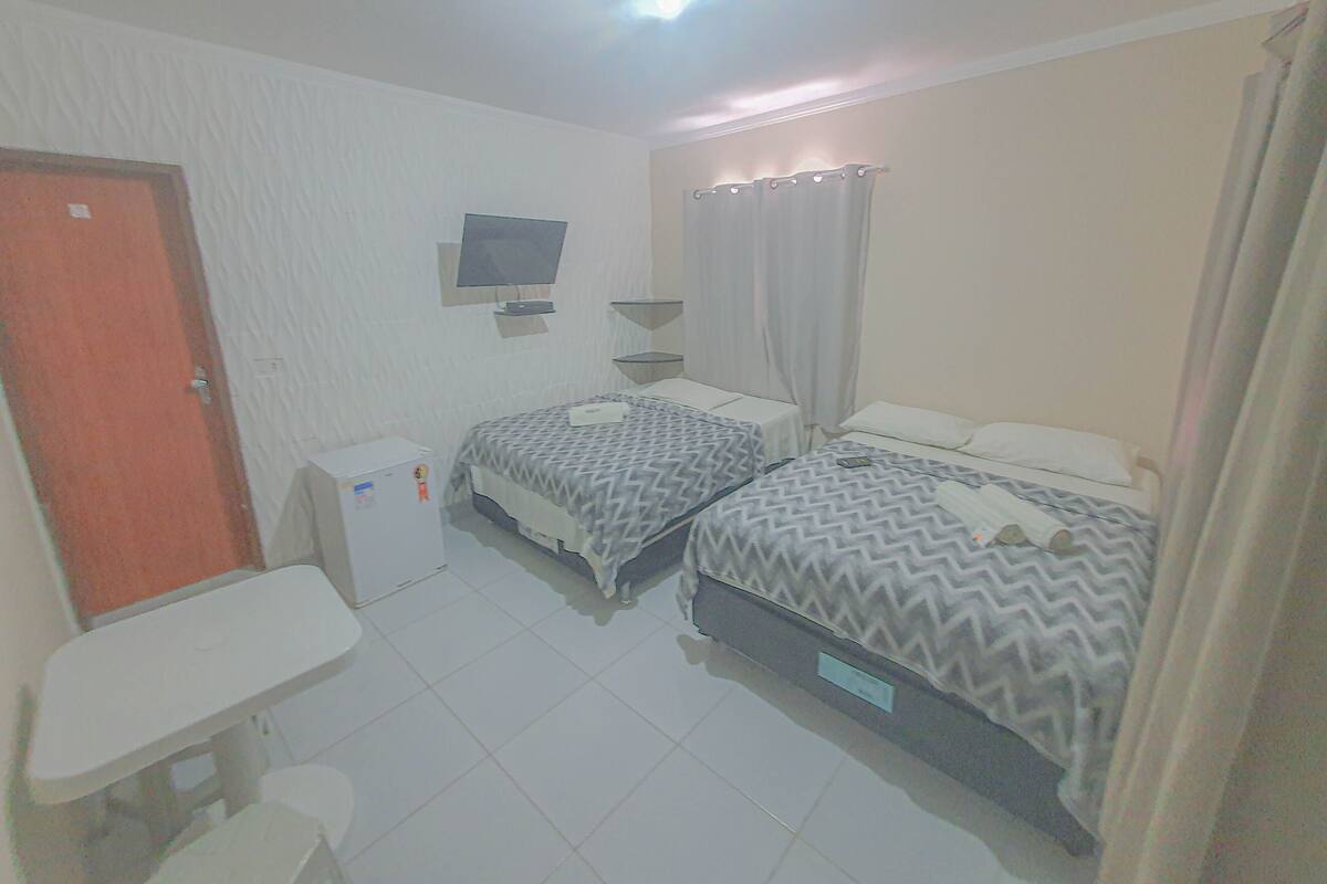 Une petite chambre propre, avec deux lits, un bureau, une télévision et un rideau de douche.