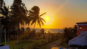 Un área de piscina con dos piscinas, rodeada por una terraza de madera, palmeras y vistas de la puesta de sol sobre el océano.
