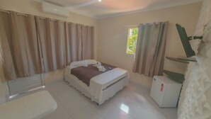 Un dormitorio con cama, un escritorio pequeño, una ventana con cortinas y un equipo de aire acondicionado.