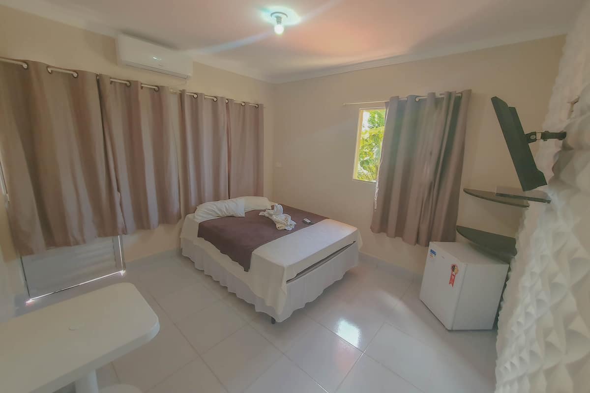 Une chambre à coucher comprenant un lit, un petit bureau, une fenêtre avec des rideaux et un appareil de climatisation.