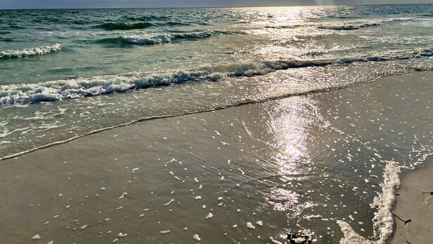 Una playa con olas lamiendo suavemente la orilla, bajo un cielo parcialmente nublado.