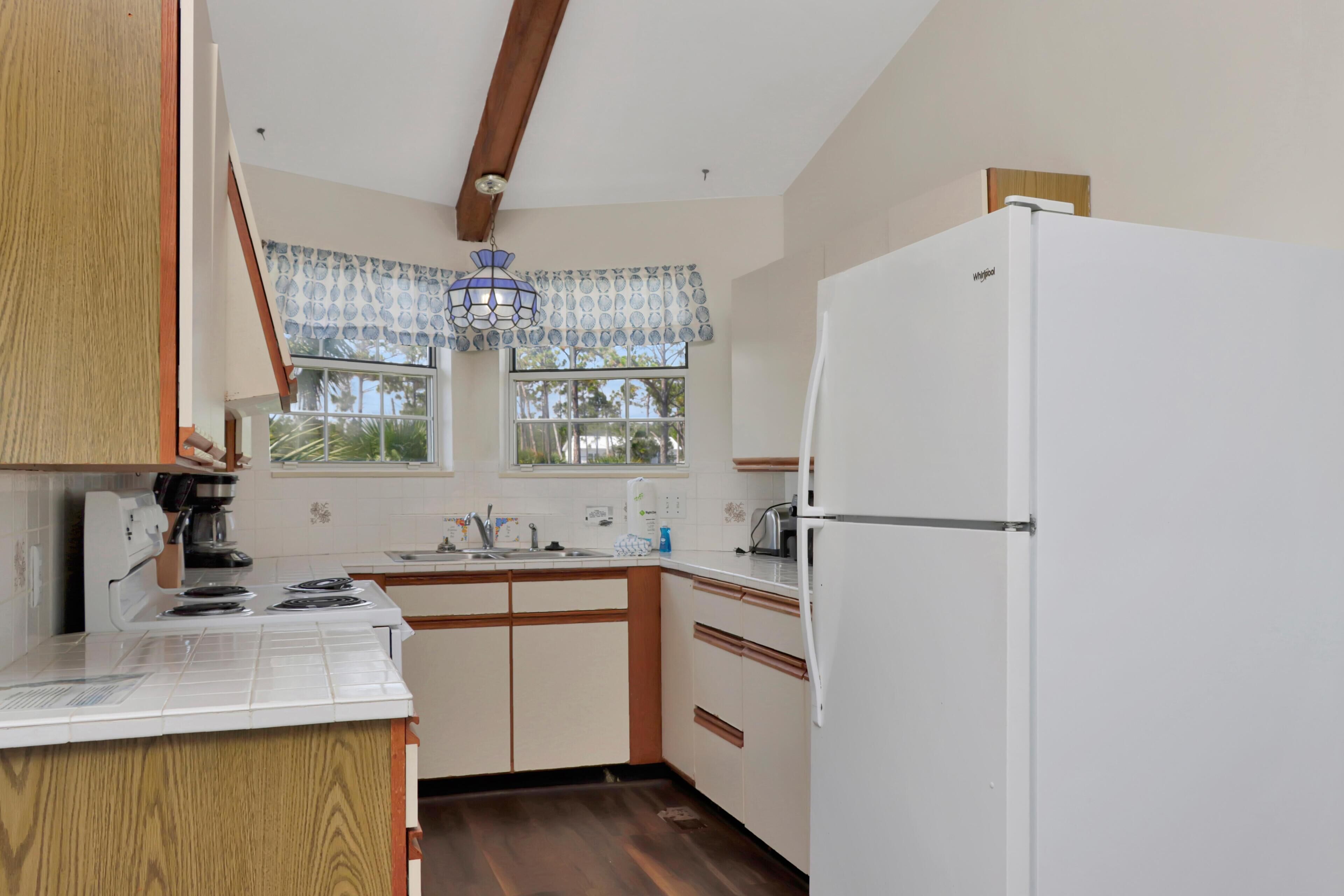 A kitchen with wooden cabinets, a white refrigerator, a stove, and a window with patterned curtains.