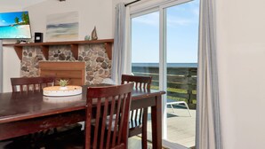 A dining area with a stone fireplace, wooden table, and chairs, overlooking a wooden deck. - Amethyst Dunes (Port St. Joe)