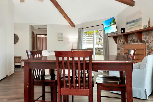 A dining area with a wooden table and chairs, a television mounted on the wall, and a stone fireplace. - Amethyst Dunes (Port St. Joe)