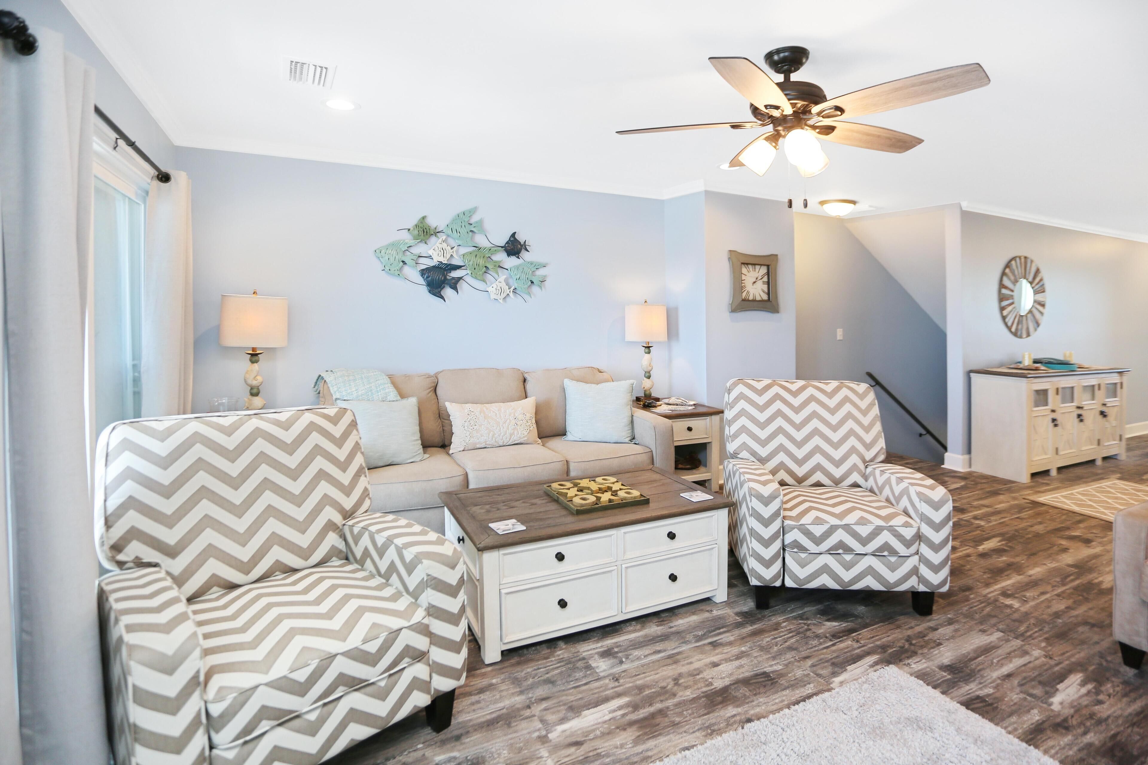 Un salon comprenant un canapé, deux fauteuils, une table basse, un ventilateur de plafond et un élément décoratif mural.