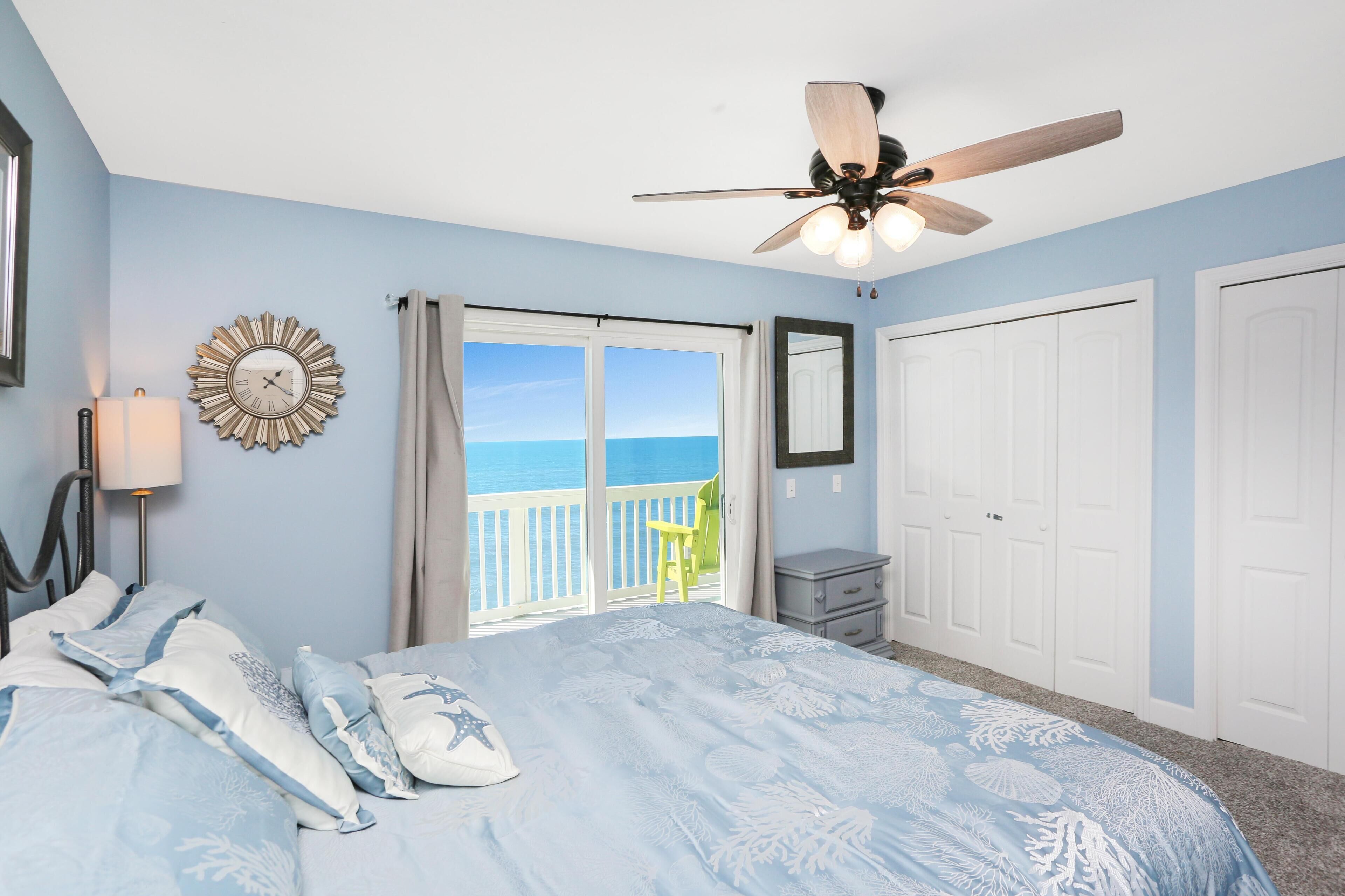 Une chambre avec un lit, un ventilateur de plafond, une horloge et une vue sur l’océan.