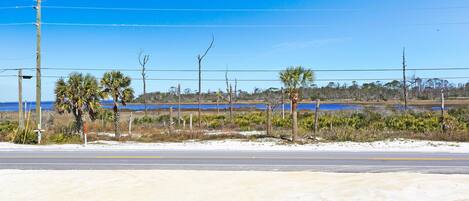A coastal road with a clear blue sky, a sandy beach, and a body of water in the distance.