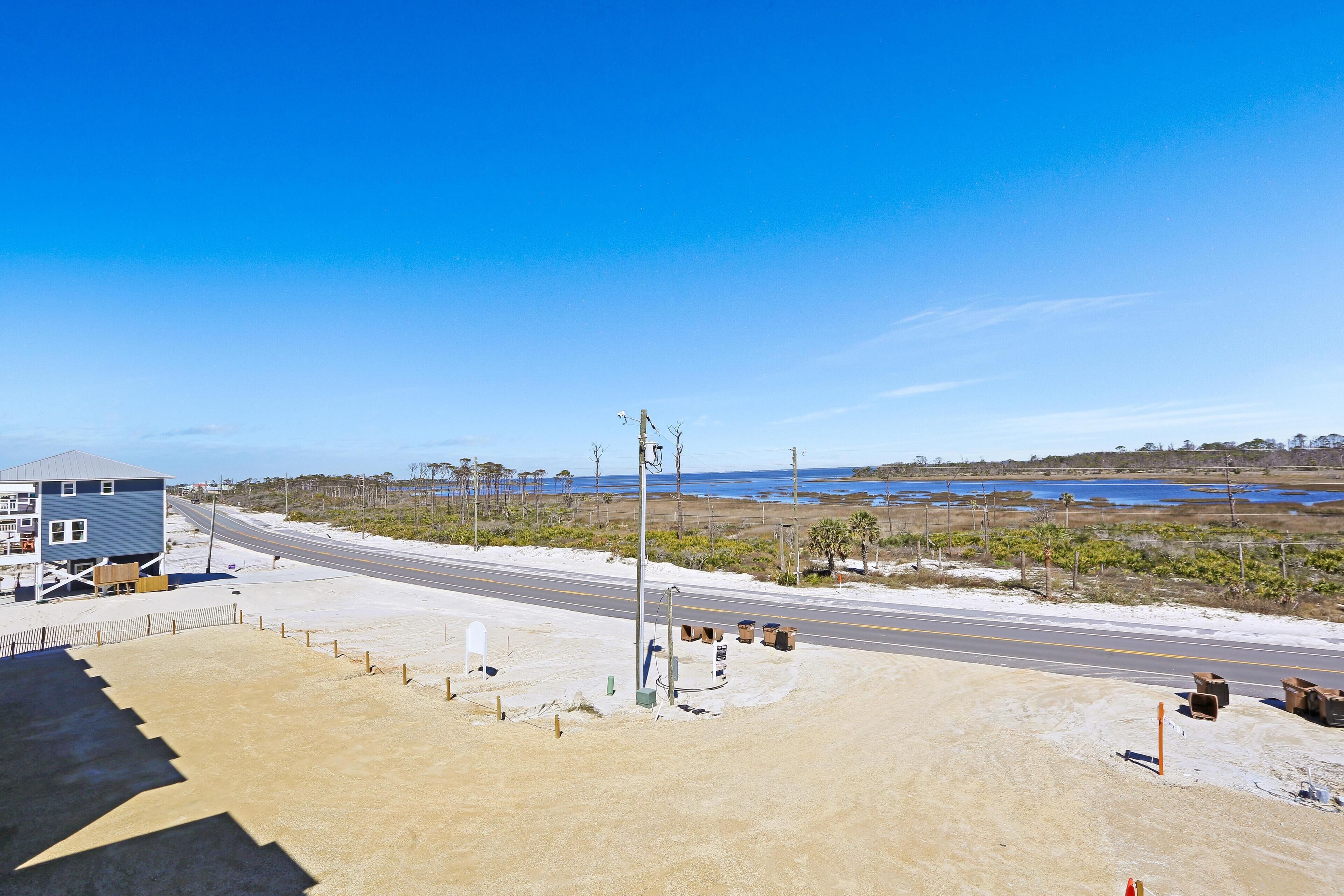 Une route côtière avec un bâtiment bleu sur la gauche, un ciel dégagé et une plage au loin.