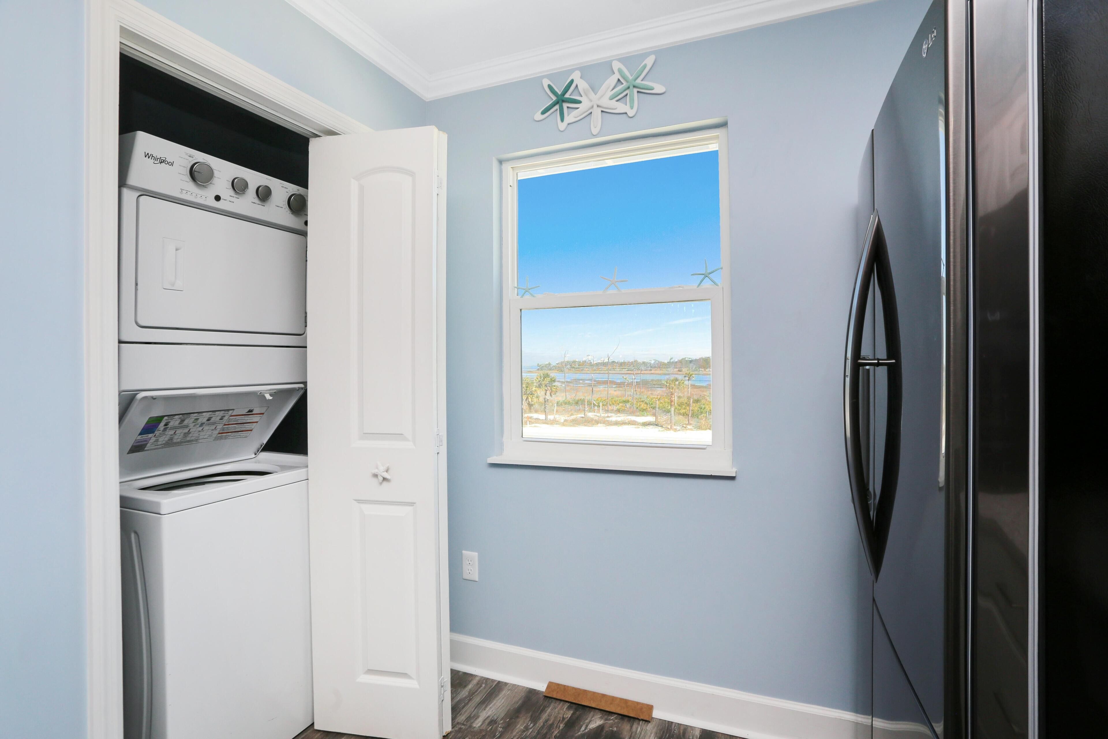 A laundry room with a washer and dryer, a window with a view, and a refrigerator.