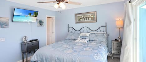 A bedroom with a bed, a ceiling fan, a TV, a framed picture, a nightstand, and a lamp.