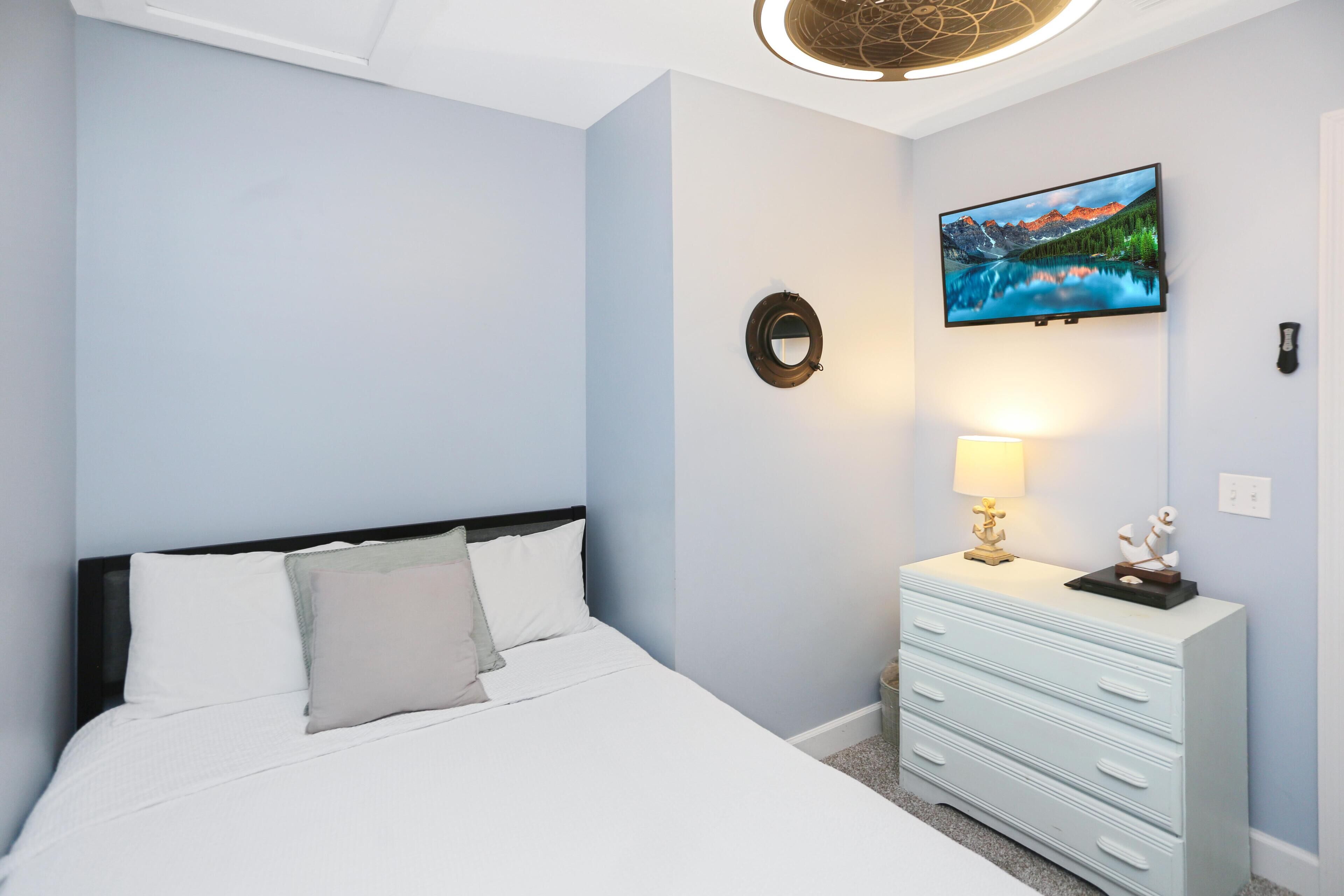 A bedroom with a bed, a dresser, a TV on the wall, and a lamp.