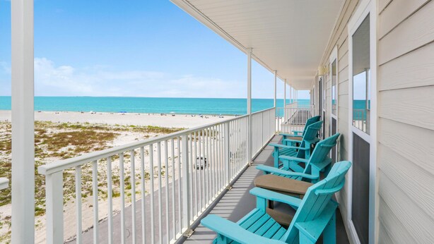 Een balkon met uitzicht op het strand, voorzien van zitplaatsen buiten en een hekwerk.