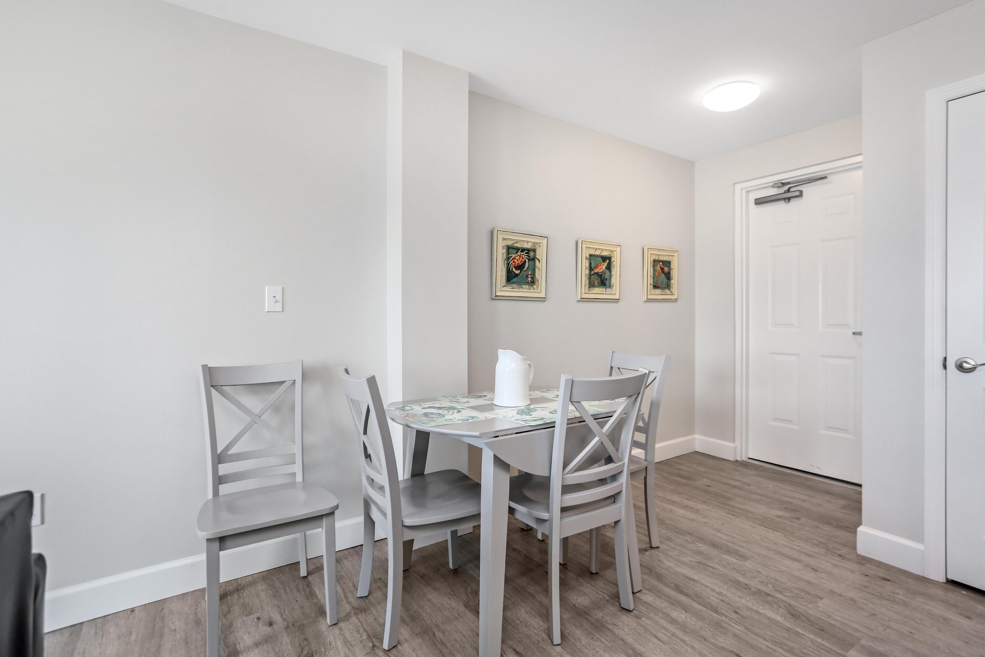 A dining area with a table and four chairs, a white door, and three framed pictures on the wall.