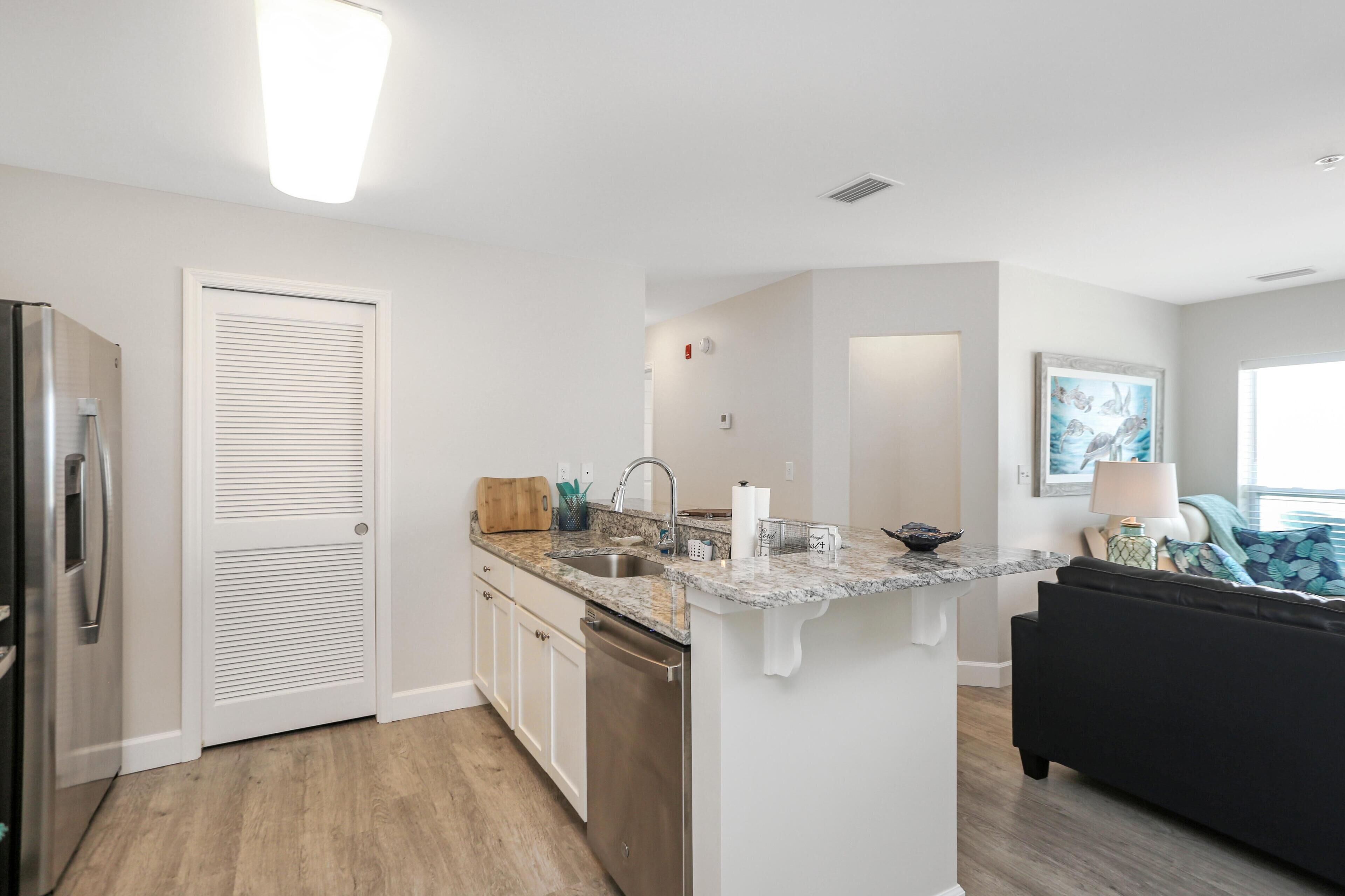 A modern kitchen with white cabinetry, a built-in dishwasher, and a granite countertop.