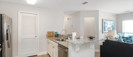 A modern kitchen with white cabinetry, a built-in dishwasher, and a granite countertop.
