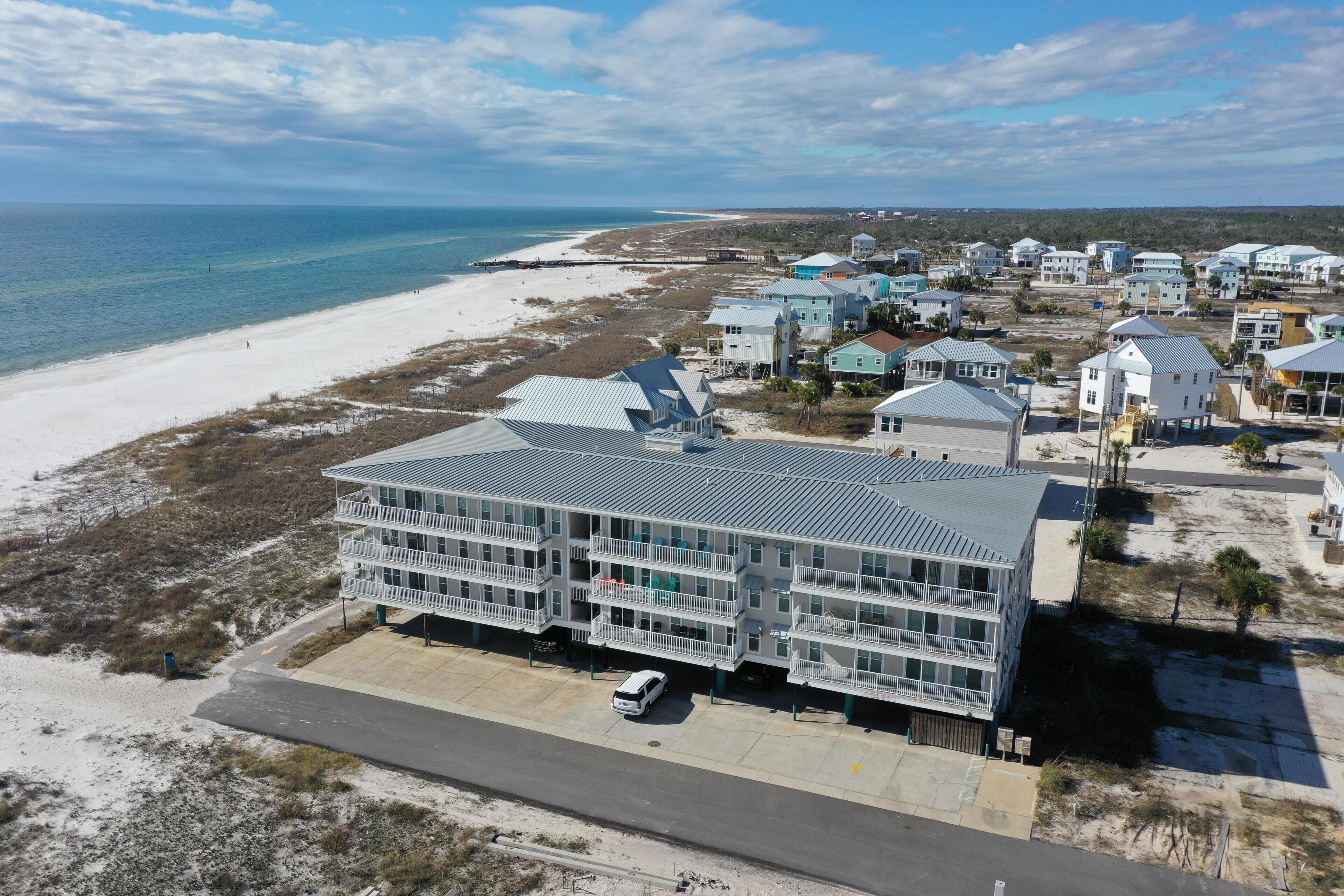 A coastal hotel with multiple balconies, a parking area, and a view of the beach and ocean.