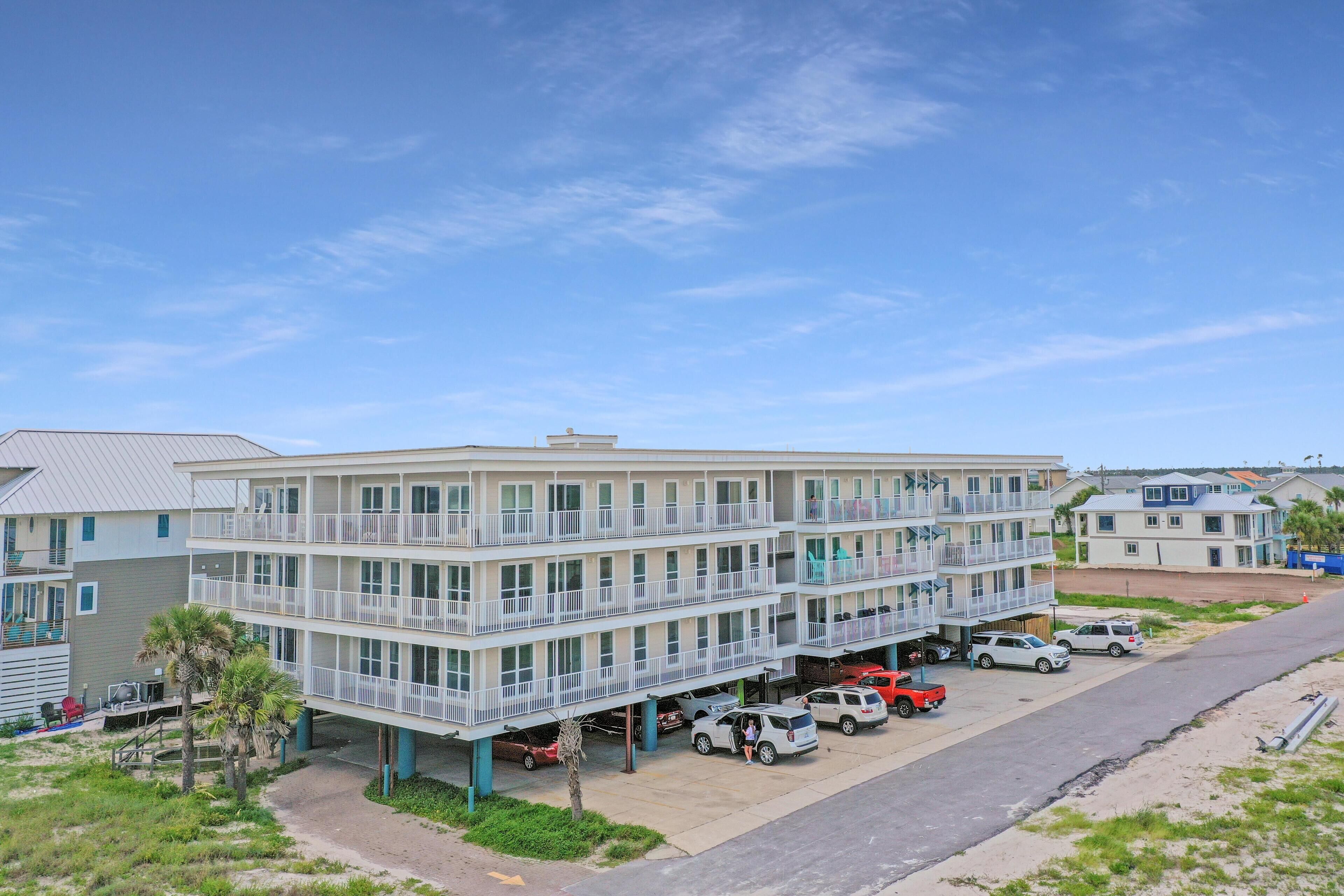 A multi-story hotel with balconies, parking, and a view of the beach.