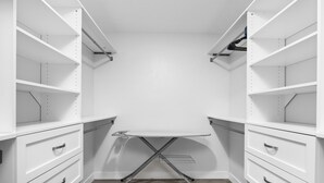 Een witte kast met open planken, een opklapbaar strijkplank en lades.