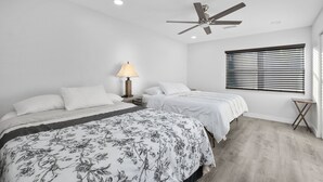 Een slaapkamer met twee bedden, een plafondventilator, een raam met jaloezieën en een bedlampje.