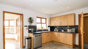 A modern kitchen with wooden cabinets, a dishwasher, and a window providing natural light. - Kilnary Cottage (Ellon)