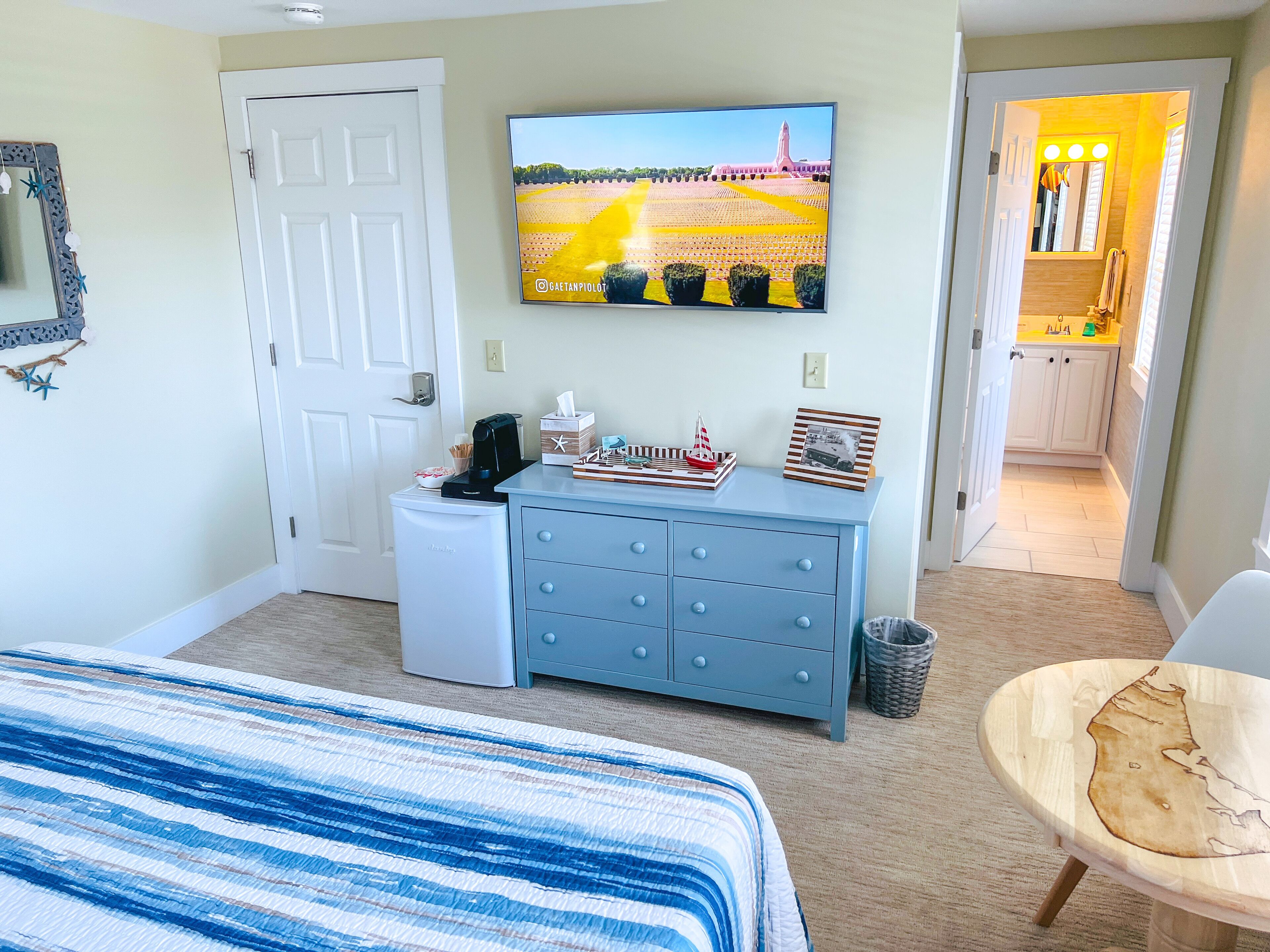 A hotel room with a bed, a dresser, a television, and a view of the kitchen.