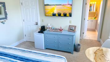 A hotel room with a bed, a dresser, a television, and a view of the kitchen.