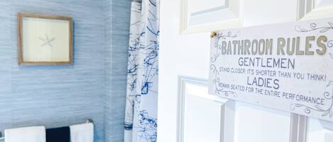 Un baño con un letrero que dice 'Normas del baño' y un perchero con la etiqueta 'Maquillaje'.