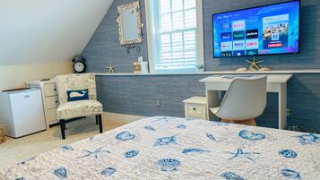 Een slaapkamer met een bed, een bureau, een stoel, een kleine koelkast, een televisie en een raam met jaloezieën.