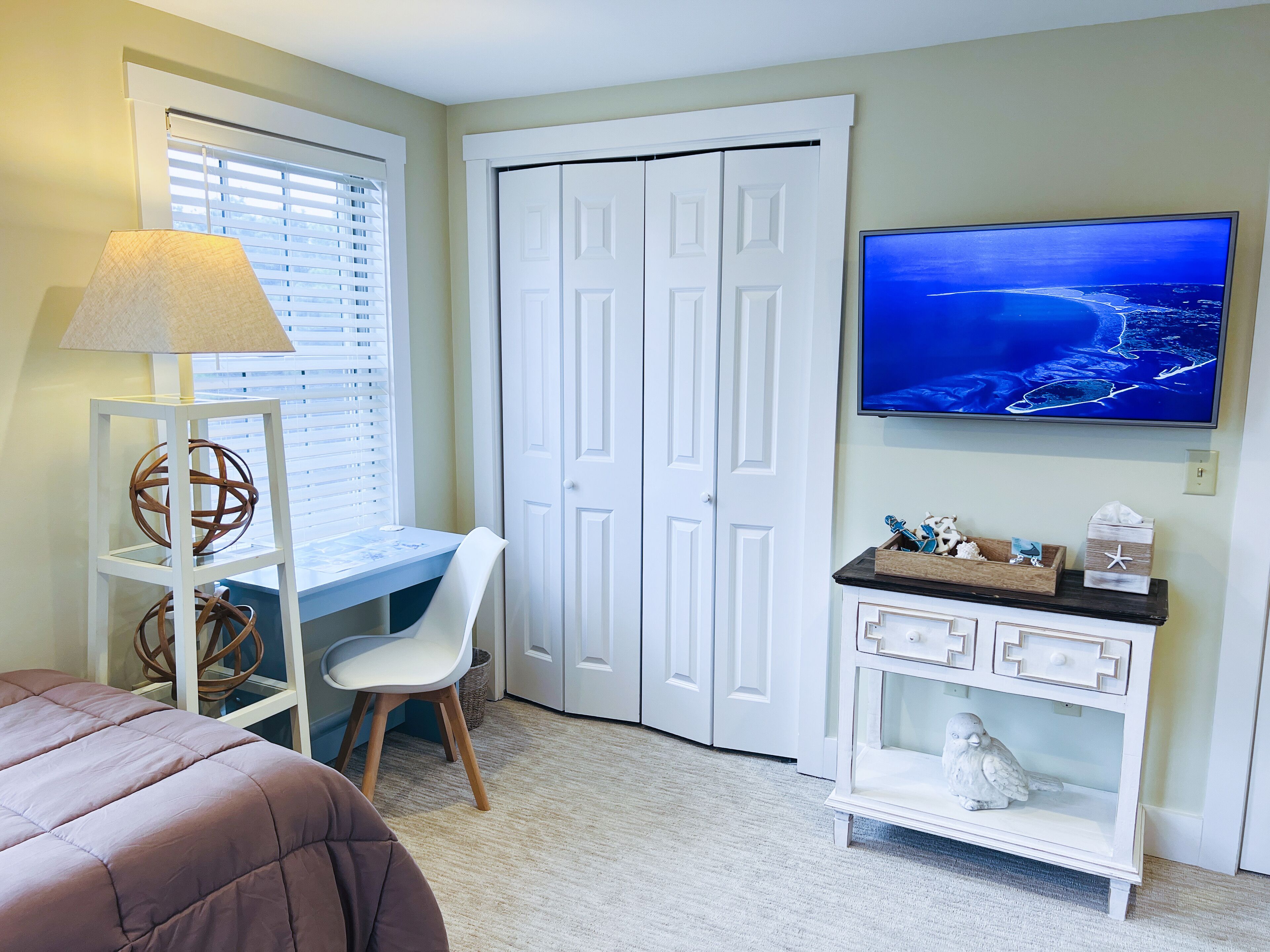 A bedroom with a bed, a desk, a chair, a TV, and a dresser.