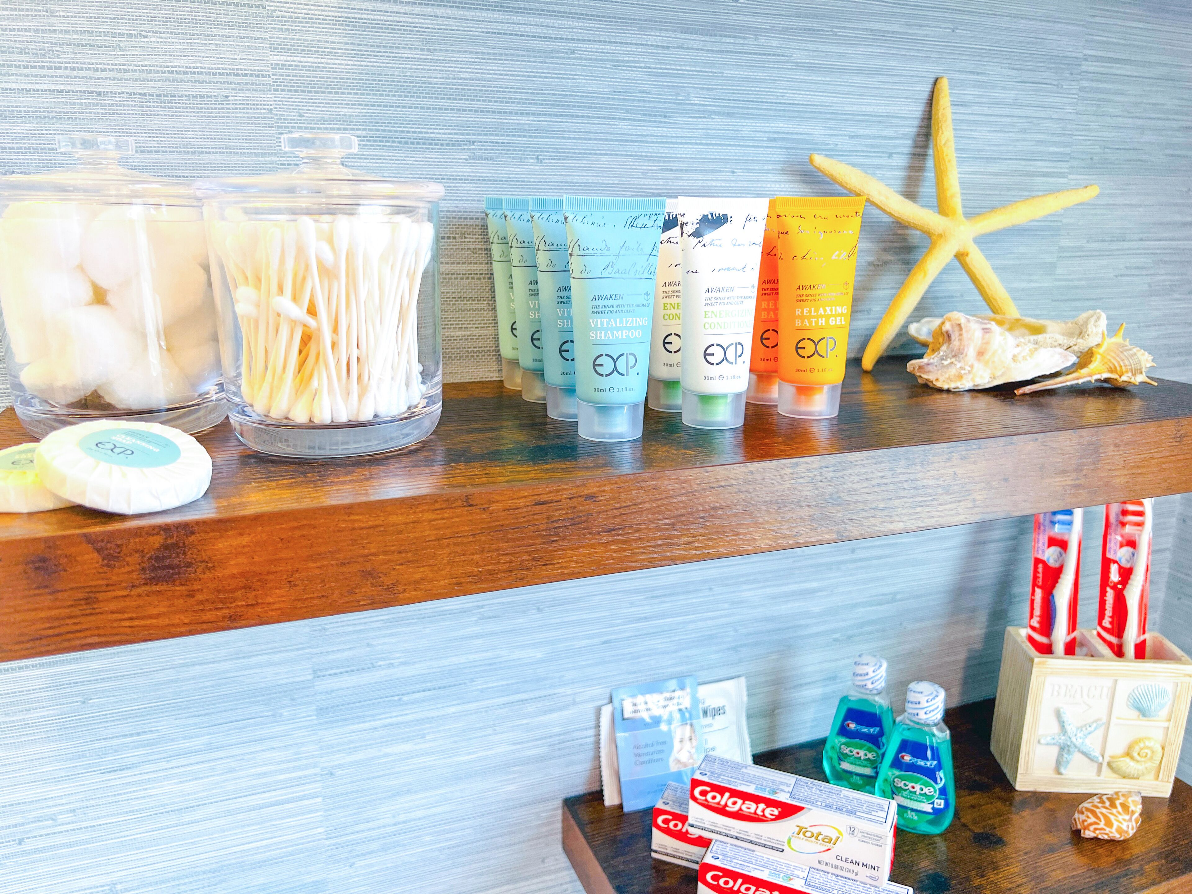 Une étagère de salle de bain contenant des articles de toilette, notamment des cotons-tiges, du shampoing, de l’après-shampoing et du dentifrice.