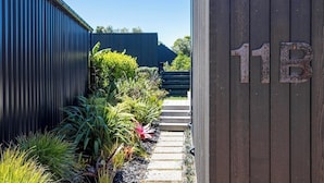 A narrow pathway leading to a building with a dark exterior and a wooden door marked with the number 11B. - 2 min walk to the glorious white sands of Onetangi beach (Waiheke Island)