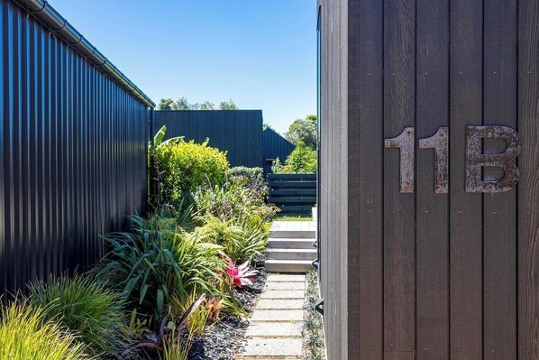 A narrow pathway leading to a building with a dark exterior and a wooden door marked with the number 11B.