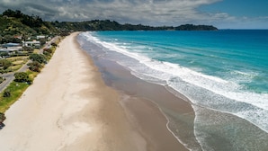 A wide beach with clear blue waters and a distant island. - 2 min walk to the glorious white sands of Onetangi beach (Waiheke Island)