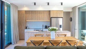 A modern kitchen with wooden cabinets, a stainless steel refrigerator, and a dining area with a wooden table and chairs. - 2 min walk to the glorious white sands of Onetangi beach (Waiheke Island)