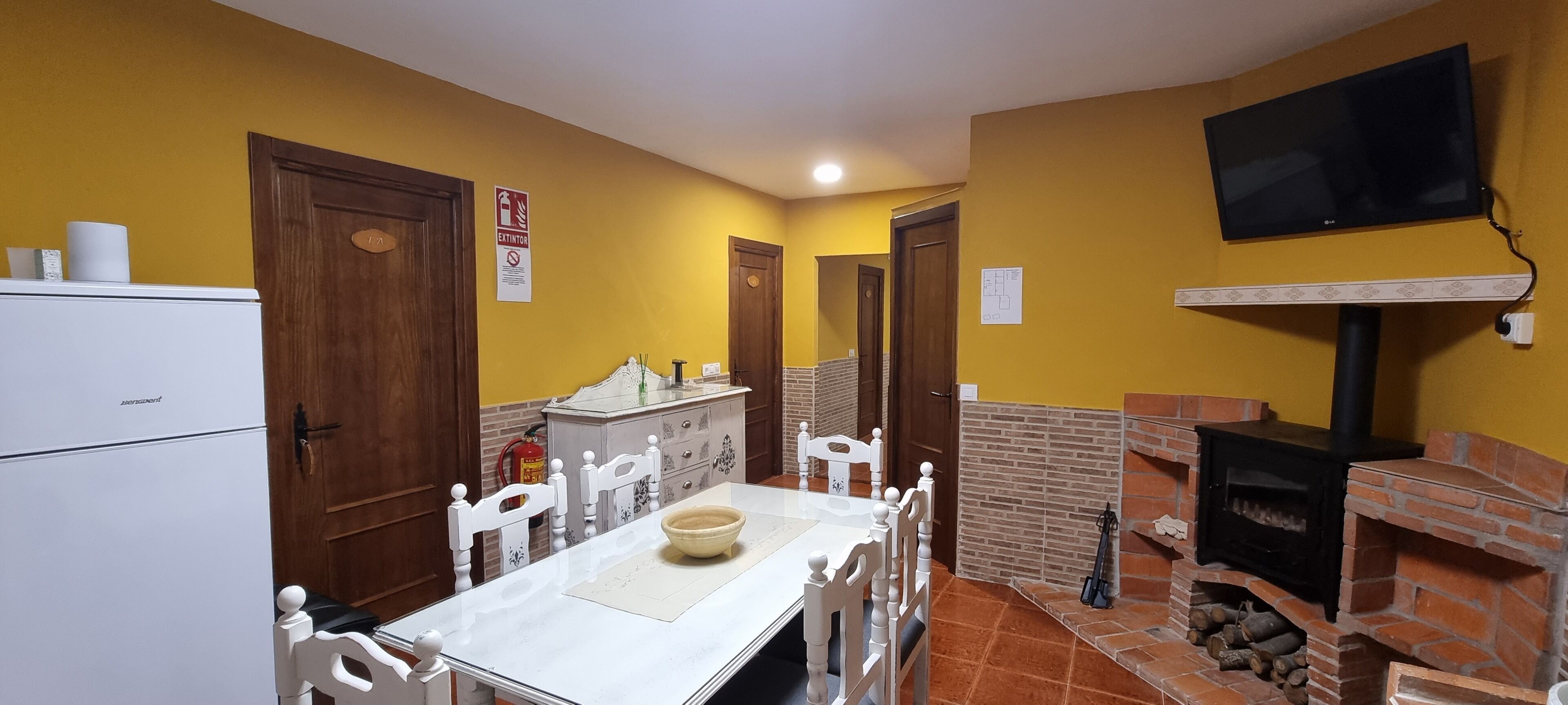 A compact kitchen with a white refrigerator, wooden cabinets, a dining table with chairs, and a brick fireplace.